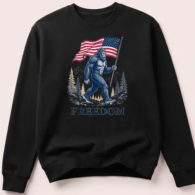 Detailed illustration of Bigfoot holding an American flag with the text FREEDOM — printed on a unisex sweatshirt