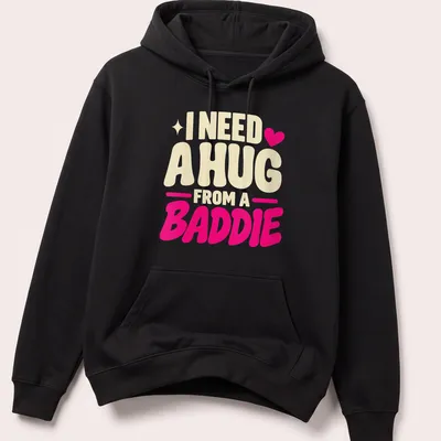 Bold playful text saying 'I Need A Hug From A Baddie' in cream, pink, and red — printed on a unisex hoodie