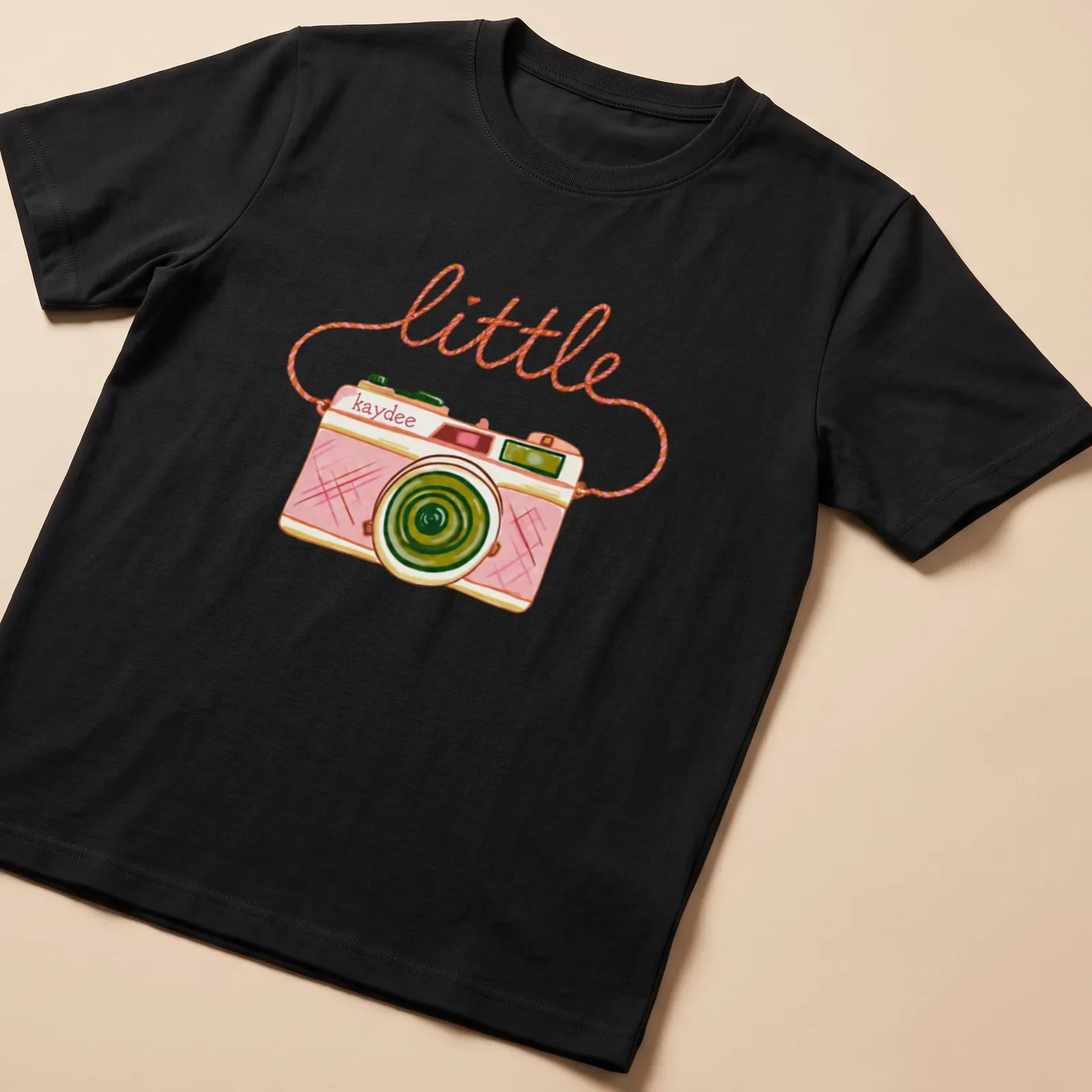 Watercolor design of a camera with the text 'little kaydee' in pink and green hues — printed on a unisex t-shirt