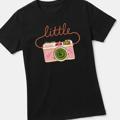 Watercolor design of a camera with the text 'little kaydee' in pink and green hues — printed on a women's shirt