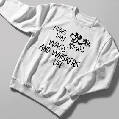 Playful line-art of a cartoon dog with the phrase 'Living That Wags And Whiskers Life' below — printed on a unisex sweatshirt