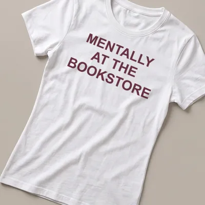 Bold typography t-shirt with the text 'Mentally At The Bookstore' in maroon and white — printed on a women's shirt