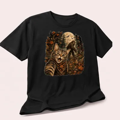 Detailed illustration of a cat taking a selfie with Sasquatch in Halloween colors — printed on a unisex t-shirt (angled view)