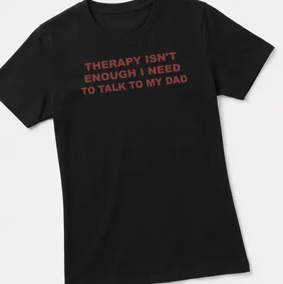 Bold typography shirt stating 'THERAPY ISN'T ENOUGH I NEED TO TALK TO MY DAD' in red on white. — printed on a women's shirt